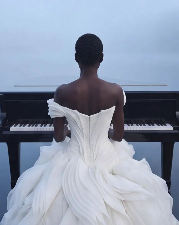 Bride in a sculptural off-shoulder ruffled gown playing a grand piano, seen from behind